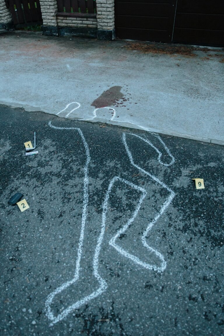 Crime scene with chalk outline and evidence markers on pavement, indicating a forensic investigation.
